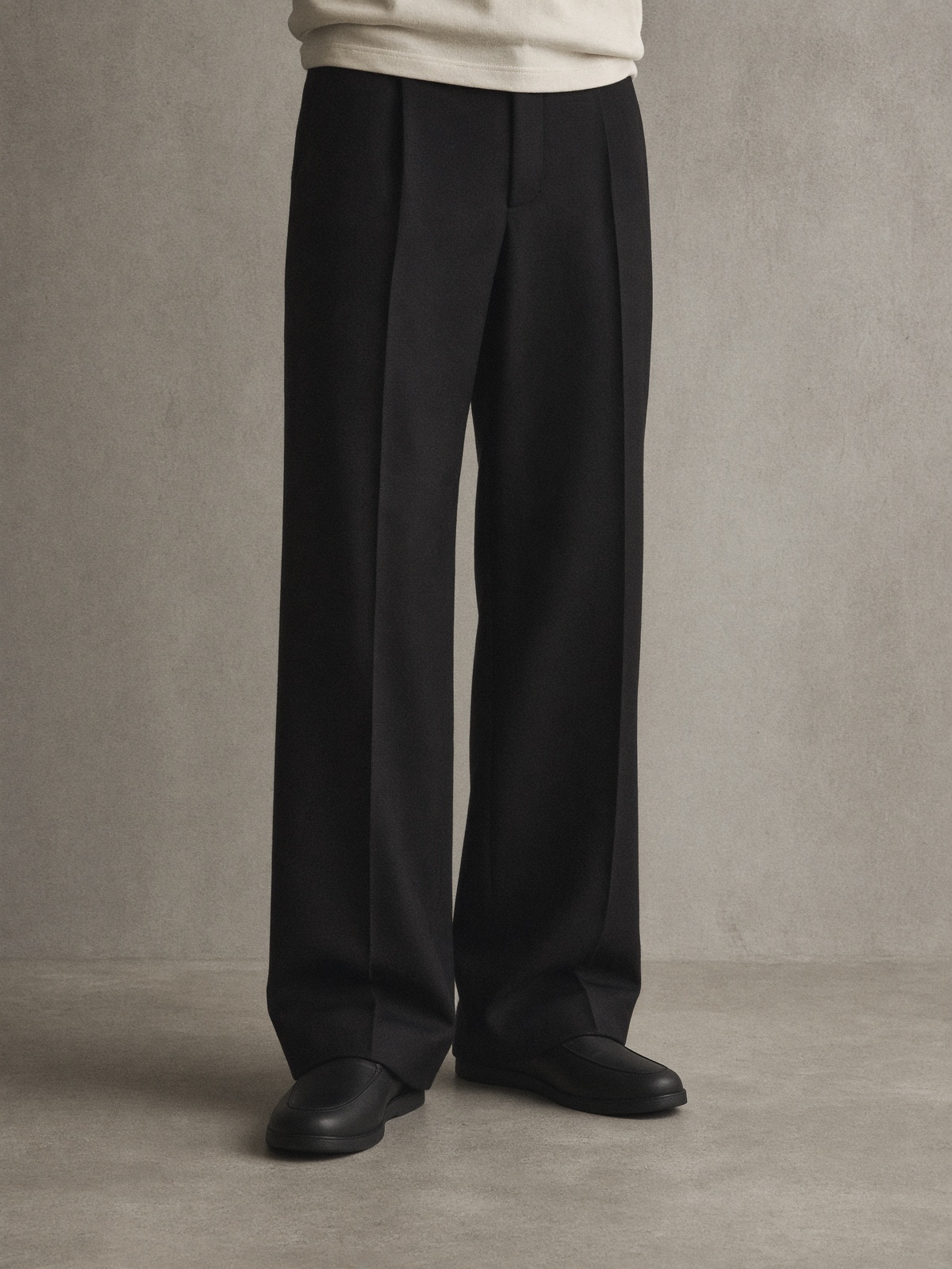 Wide black wool trousers breaking over matte black slip shoes.